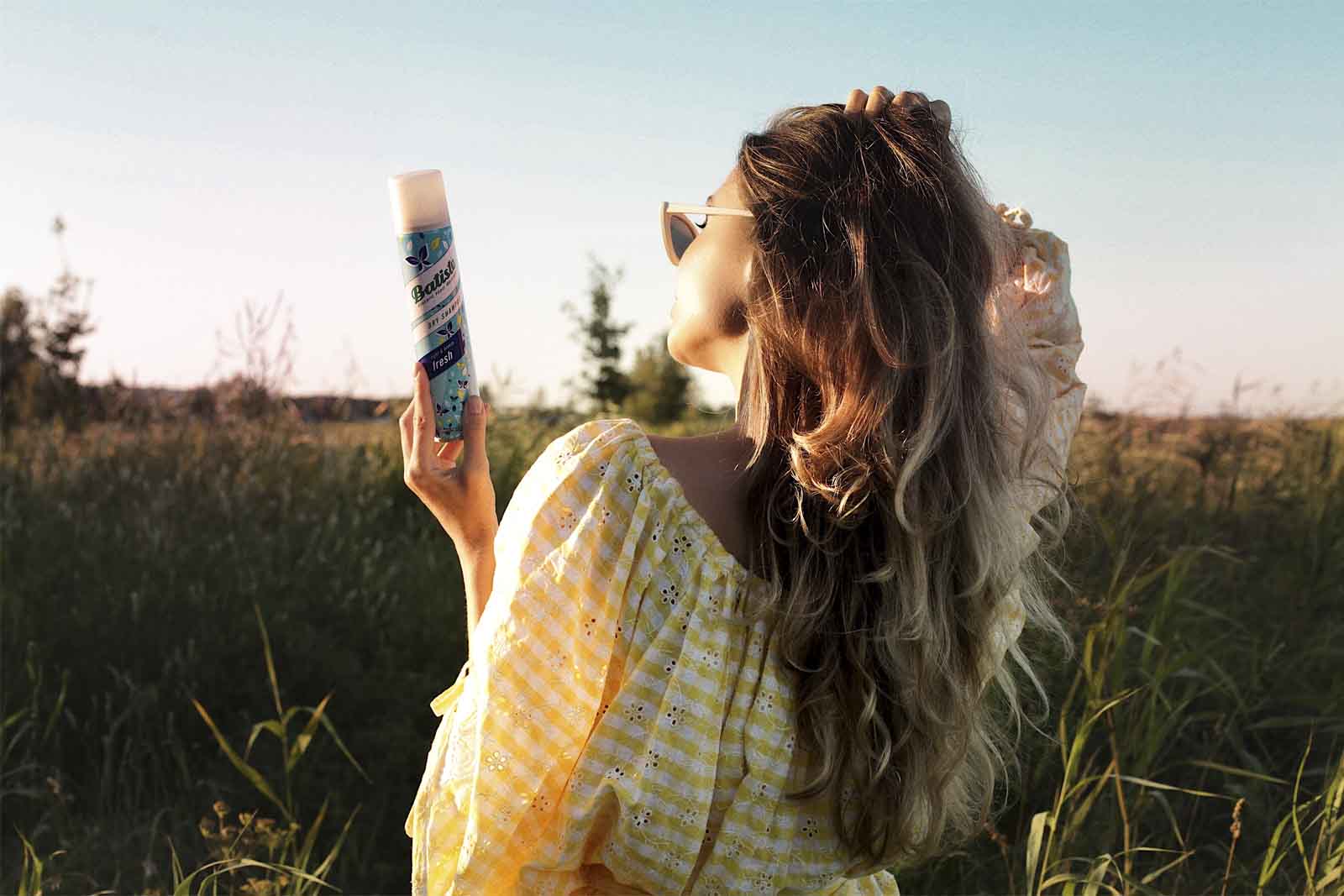 Chica de pelo largo de espaldas en el campo, sujetando un champú en seco Batiste Fresh