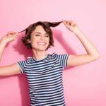 Chica sonriente con camiseta de rayas tocándose el pelo, con un corte de pelo bob a capas