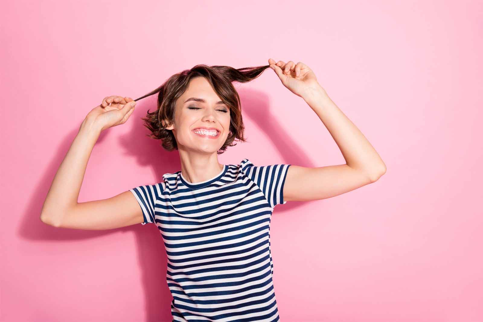 Chica sonriente con camiseta de rayas tocándose el pelo, con un corte de pelo bob a capas