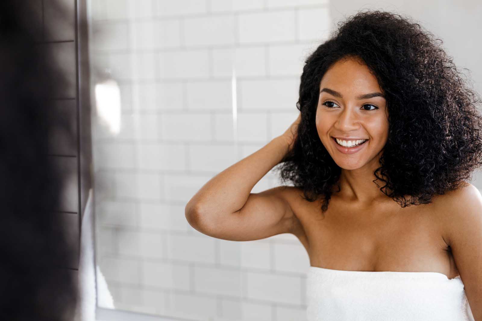 Mujer negra con pelo rizado afro mirándose al espejo después de aplicarse una mascarilla casera para pelo encrespado 