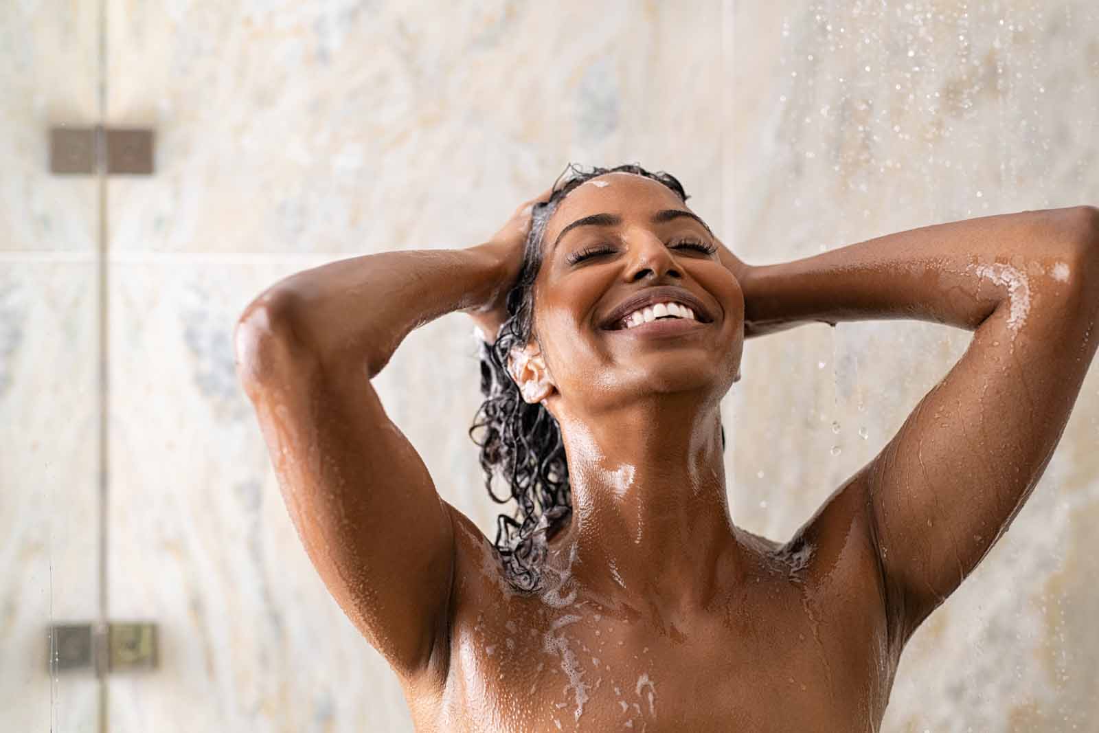 Mujer de pelo afro lavándose el pelo en la ducha
